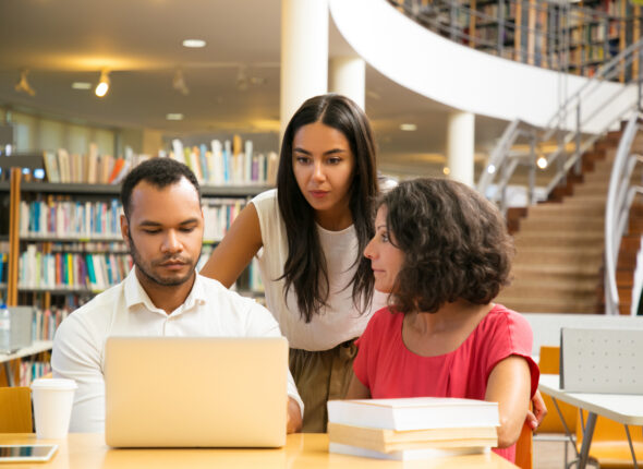 Serious students sitting at table in library working with laptop